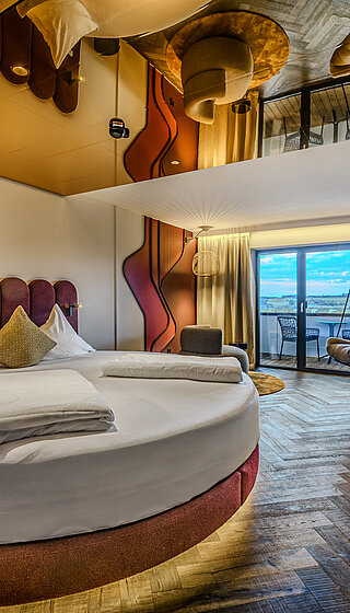 Schlafbereich mit Rundbett und Hängesessel Secret Love Suite im Hotel Winzer mit rundem Doppelbett, Hängesessel, gemütlichem Wohnbereich und Balkon