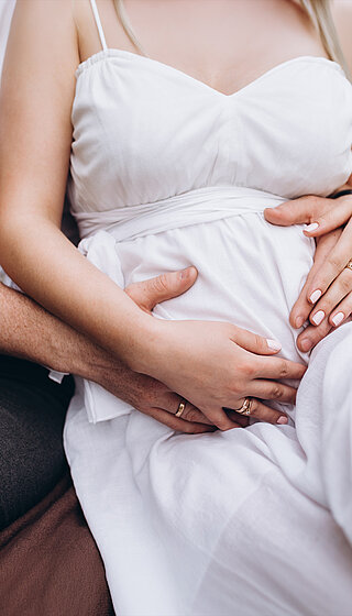 A pregnant woman and her husband embracing her bump