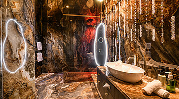 Bathroom in the Kuscheltraum Deluxe Junior Suite Luxurious vanity area in the Kuscheltraum Deluxe Junior Suite at Hotel Winzer with natural stone, an illuminated mirror and crystal detailing