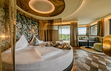 Schlafbereich der Hideaway Suite im Hotel Winzer mit rundem Doppelbett, gemütlichem Wohnbereich, Balkon und freistehendem Kamin