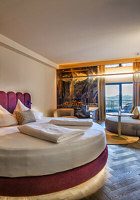 Schlafbereich der Juniorsuite Kuscheltraum Deluxe Schlafbereich der Juniorsuite Kuscheltraum Deluxe im Hotel Winzer mit rundem Doppelbett, Kamin, Sitzecke und Balkon