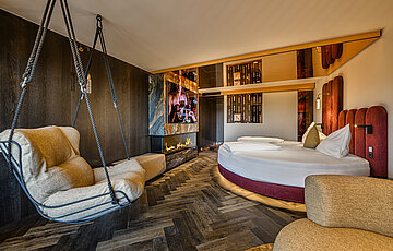 Schlafbereich der Secret Love Suite im Hotel Winzer mit rundem Doppelbett, Hängesessel und modernem Kamin