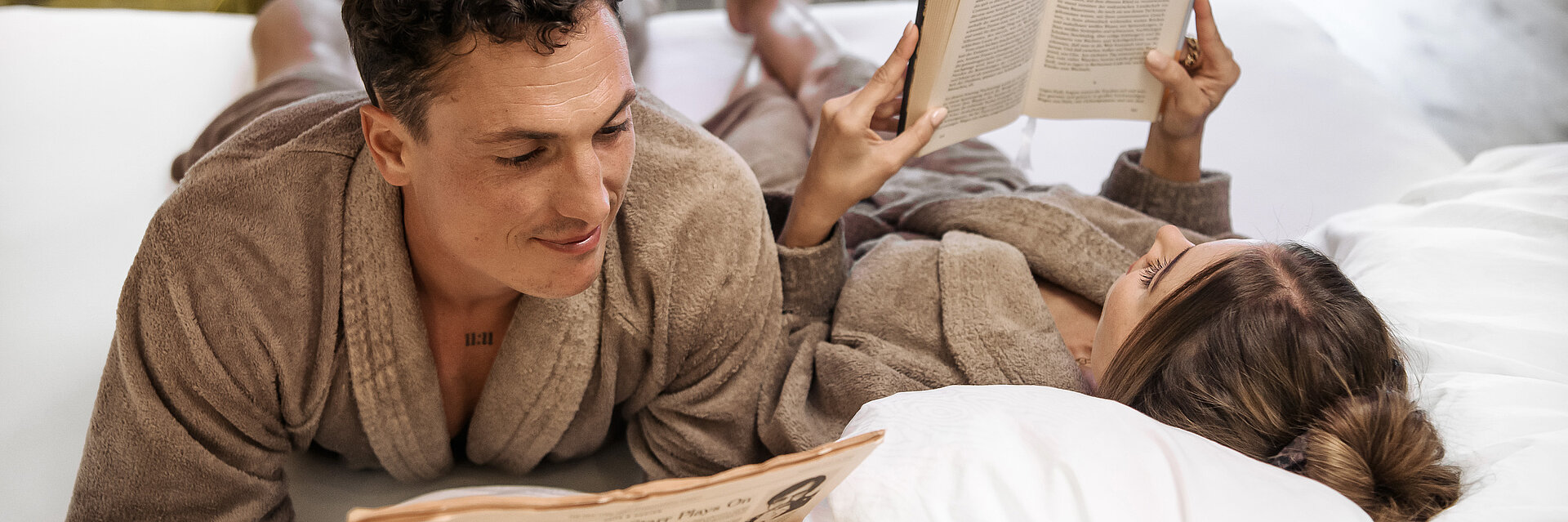 Pärchen liegt morgens im Bett und liest im Romantik-Wellnesshotel Winzer