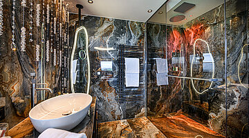 Badezimmer der Hideaway Suite Badezimmer der Hideaway Suite im Hotel Winzer mit Naturstein, elegantem Waschtisch, beleuchtetem Spiegel und großzügiger Glasdusche